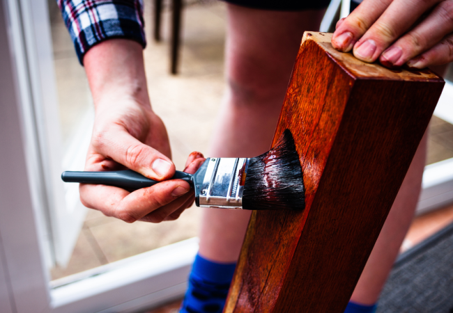 personne qui applique du vernis sur un bout de bois